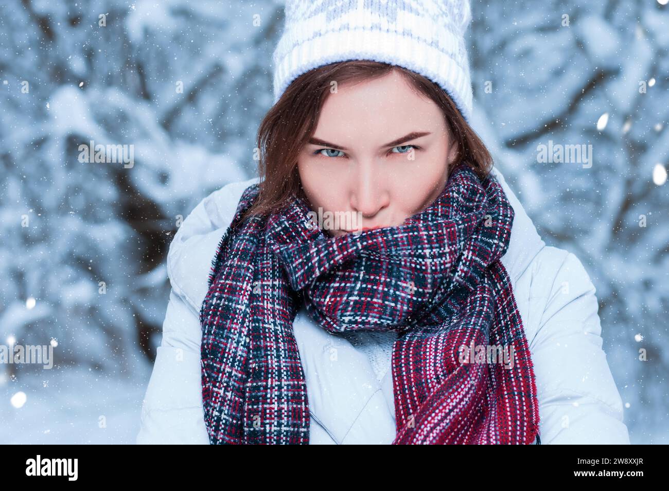 Belle fille avec une expression mécontente sur le fond d'arbres enneigés. Jeu de boules de neige. Concept de vacances de Noël. Supports mixtes Banque D'Images