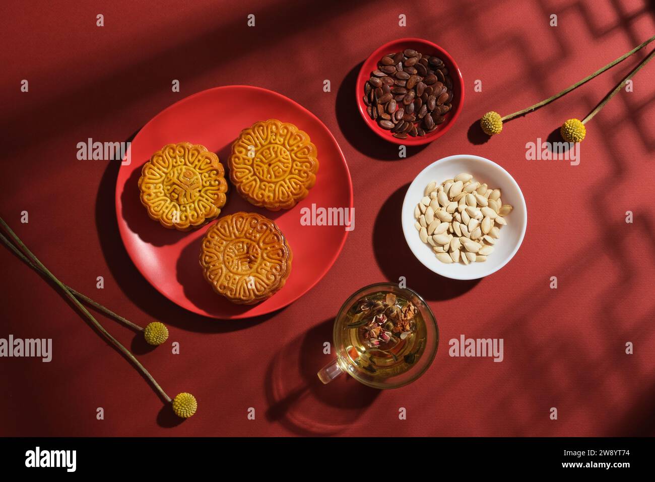 Sur un fond rouge avec des ombres de fenêtre traditionnelles, des plats en céramique remplis de délicieux gâteaux de lune, de graines de pastèque et de graines de citrouille décorées de t Banque D'Images