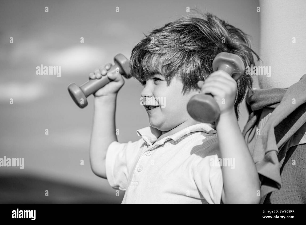 Fitness, santé et énergie. Garçon joyeux faire des exercices avec des haltères. Fitness enfant. Enfant faisant de l'exercice avec des haltères. Sport pour les petits enfants. Noir Banque D'Images