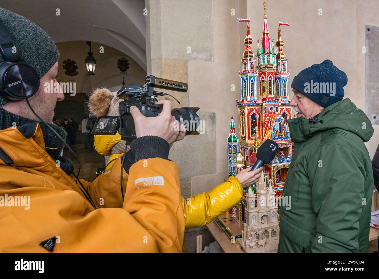 Journaliste, camescope, interviewant l'artiste à sa Szopka (scène de la Nativité de Noël) exposée à l'ouverture du concours annuel en décembre, événement inclus dans la liste du patrimoine culturel de l'UNESCO, aux arcades de Sukiennice (salle des vêtements), place principale du marché, Kraków, Pologne Banque D'Images