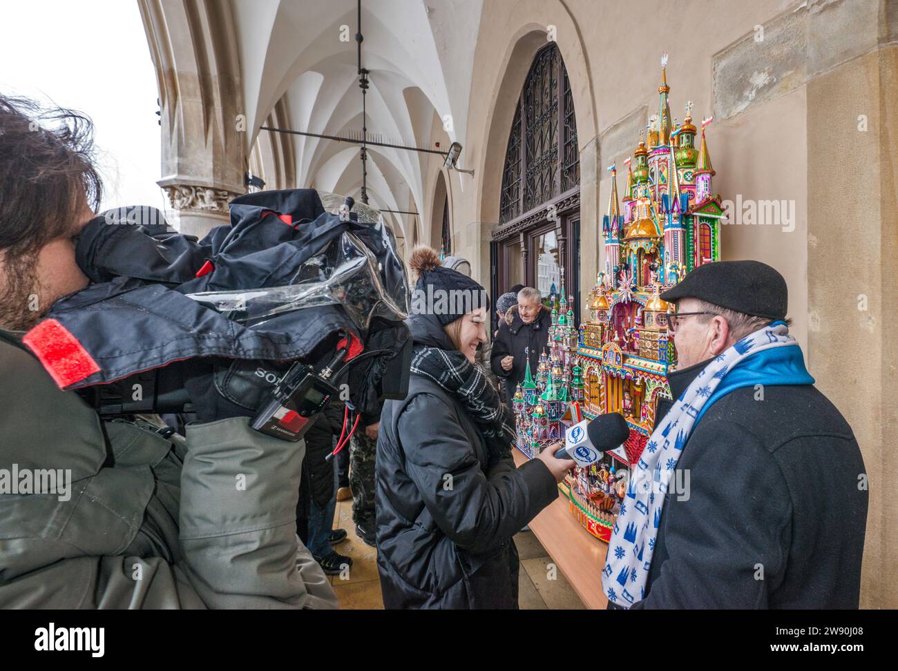 Journaliste, camescope, interviewant l'artiste à sa Szopka (scène de la Nativité de Noël) exposée à l'ouverture du concours annuel en décembre, événement inclus dans la liste du patrimoine culturel de l'UNESCO, aux arcades de Sukiennice (salle des vêtements), place principale du marché, Kraków, Pologne Banque D'Images