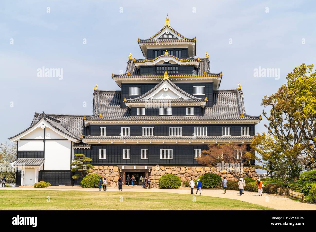 Le donjon noir reconstitué en béton, tenshu, du château d'Okayama avec ses fenêtres blanches à volets lors d'une journée ensoleillée de printemps avec un ciel bleu derrière. Banque D'Images