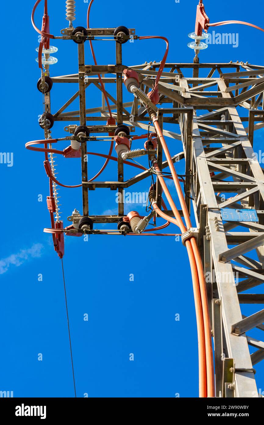 Sommet d'une tour de ligne électrique avec des câbles et des détails rouges, vu de dessous, avec ciel bleu. Image verticale Banque D'Images