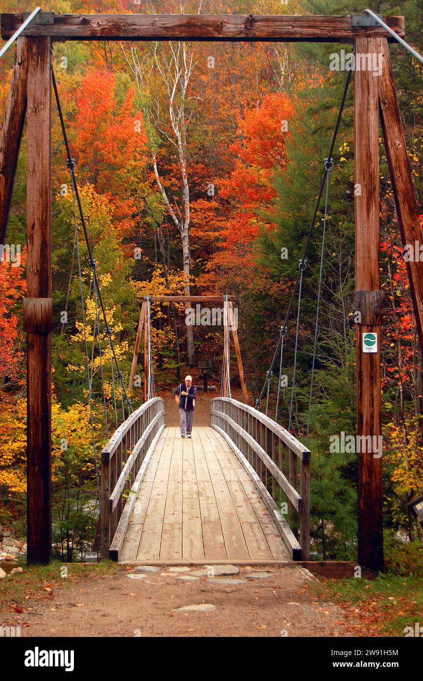 Une personne âgée active marche sur un pont suspendu piéton pour admirer les couleurs automnales des White Mountains du New Hampshire un jour d'automne en Nouvelle-Angleterre Banque D'Images