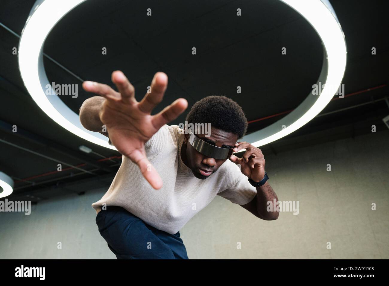 Jeune homme avec un regard futuriste à travers les cyber-lunettes sous la lampe annulaire moderne atteignant la main Banque D'Images