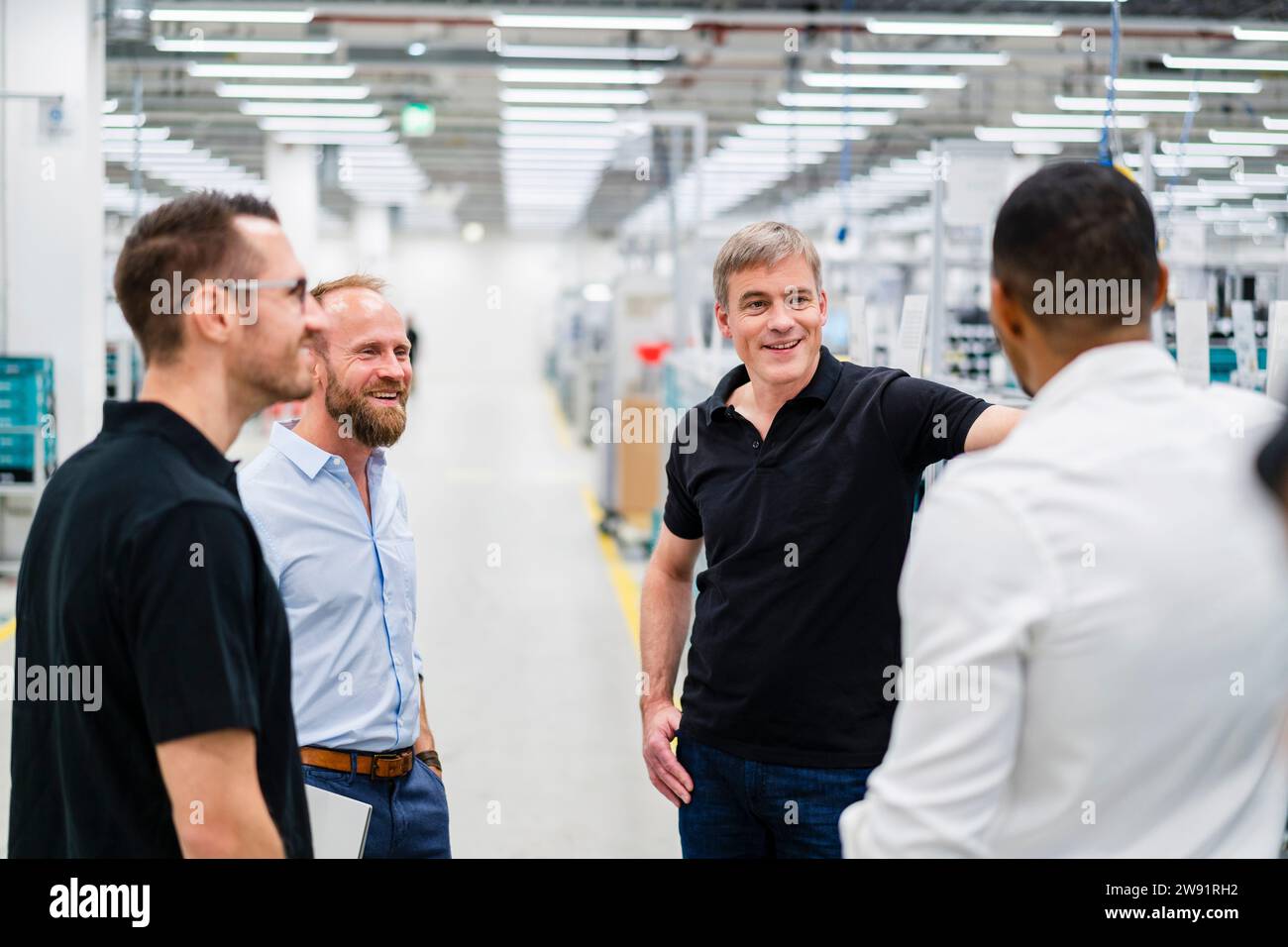 Homme d'affaires souriant et employés parlant dans une usine Banque D'Images