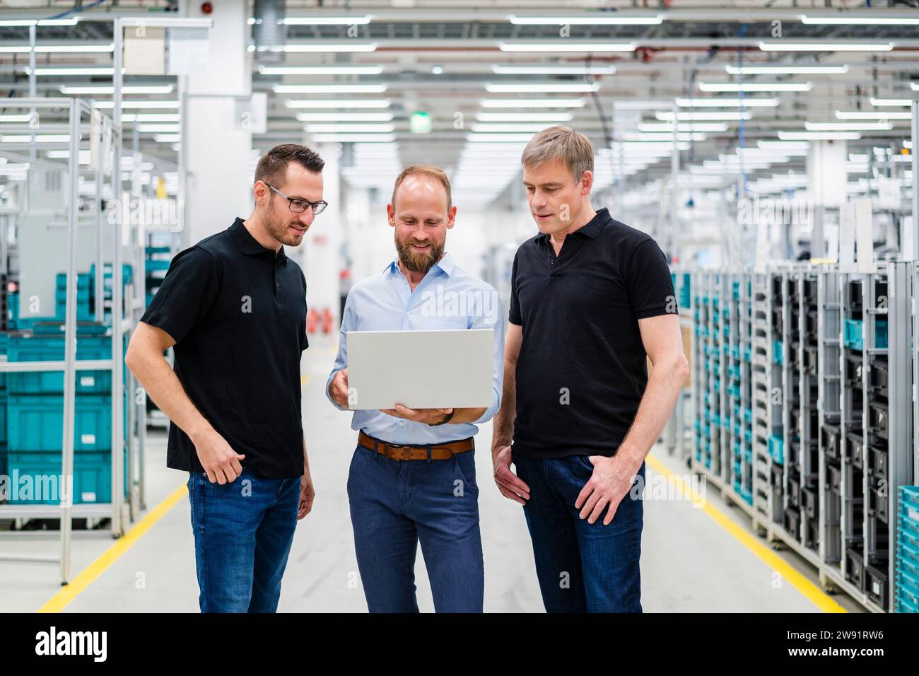 Homme d'affaires partageant un ordinateur portable avec des employés dans une usine Banque D'Images