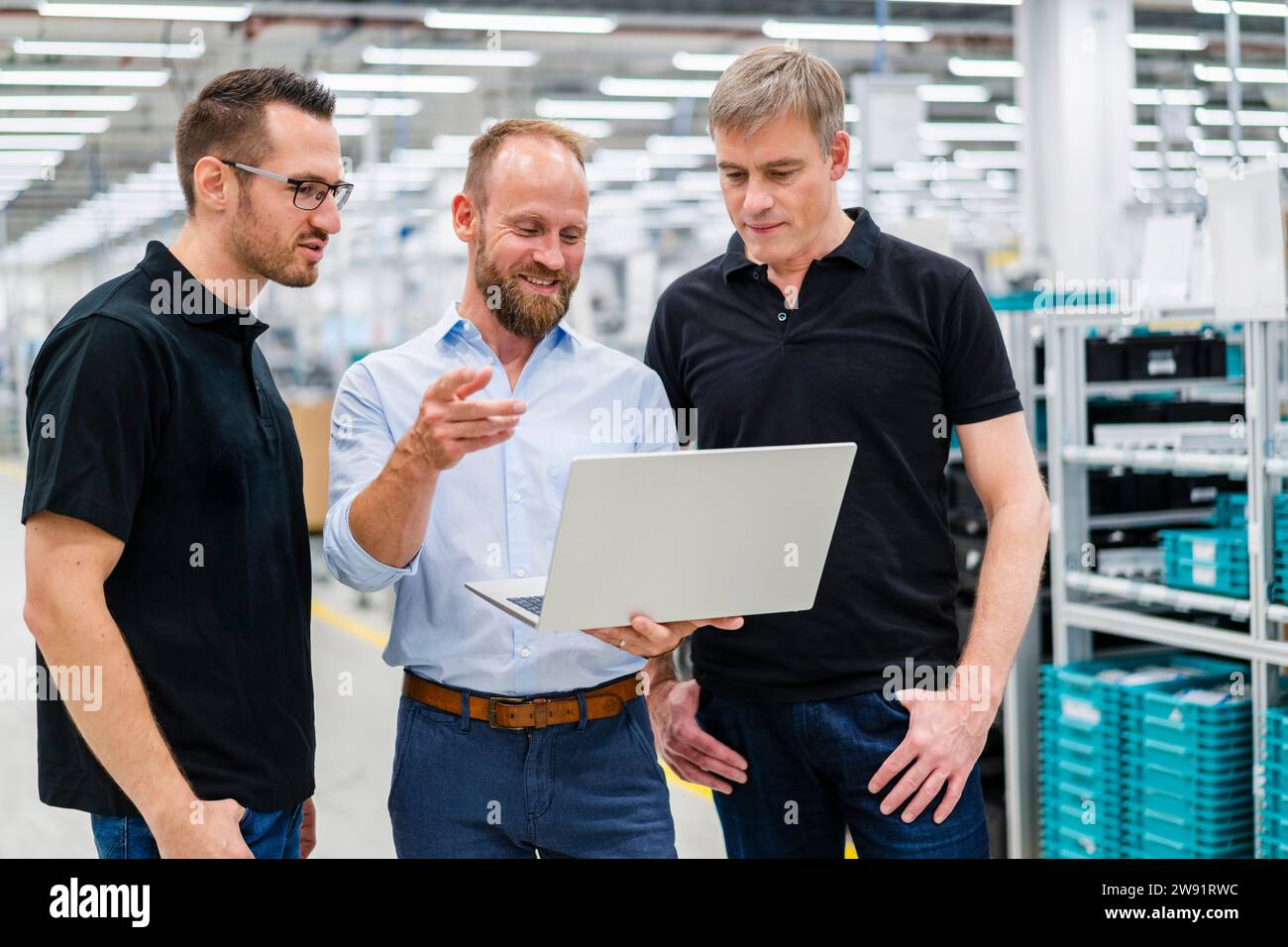 Homme d'affaires partageant un ordinateur portable avec des employés dans une usine Banque D'Images
