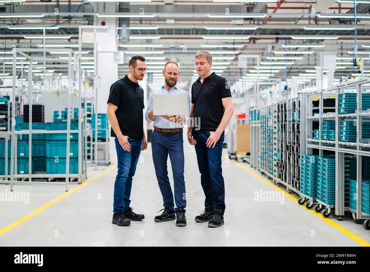 Homme d'affaires partageant un ordinateur portable avec des employés dans une usine Banque D'Images