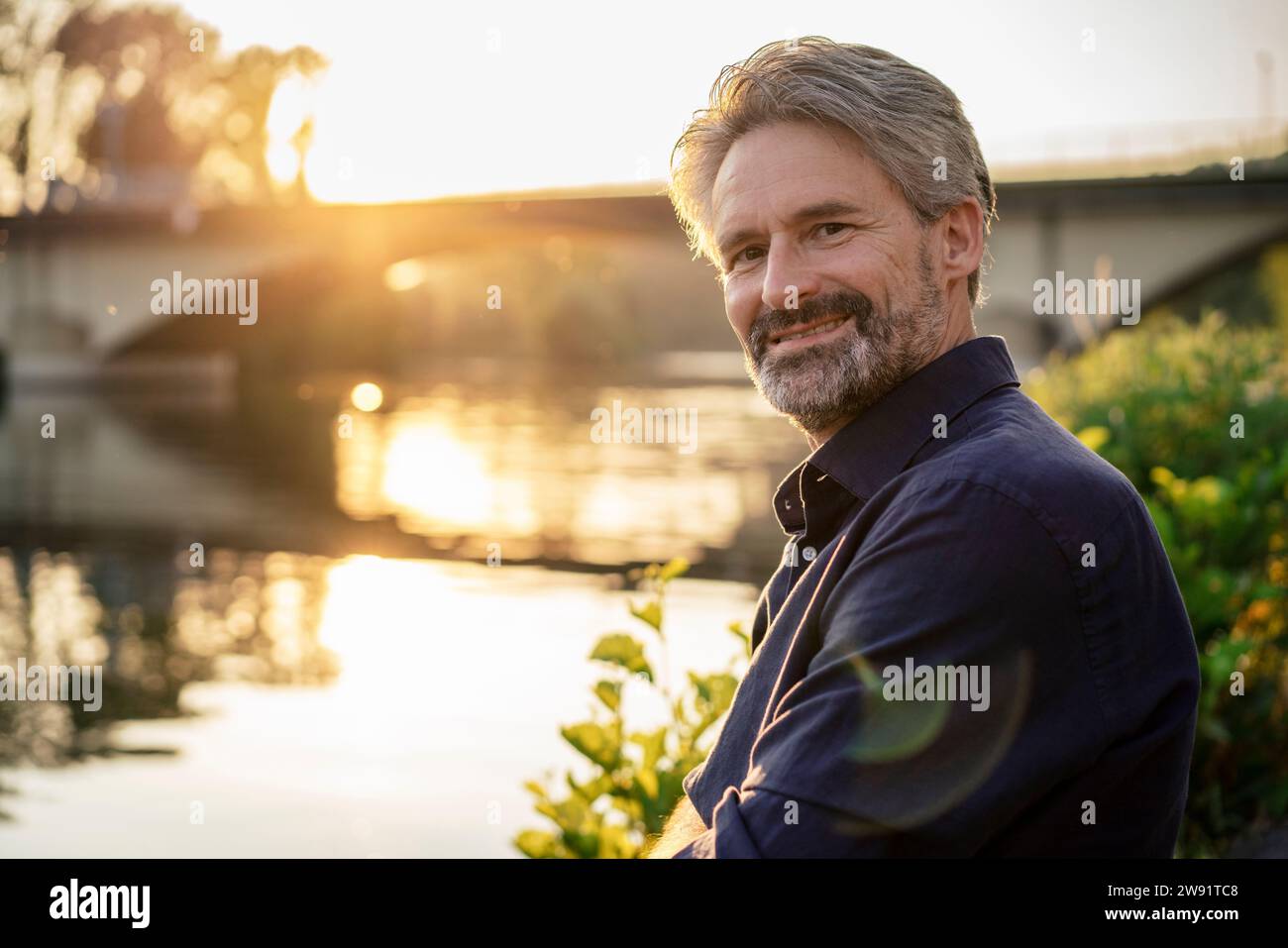 Homme souriant près du lac au coucher du soleil Banque D'Images