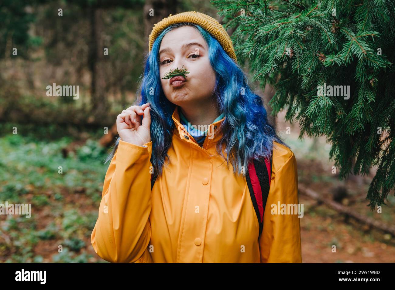 Femme portant une veste et équilibrant la brindille sur les lèvres dans la forêt Banque D'Images
