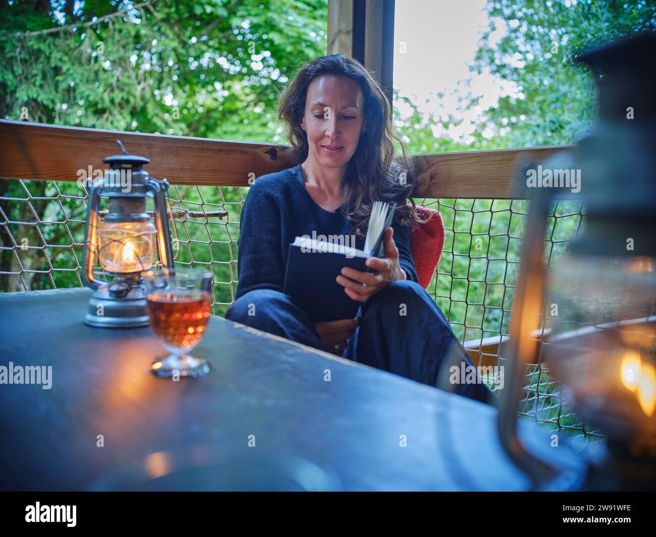 Femme mature lisant le livre près de la lampe à huile sur le porche Banque D'Images