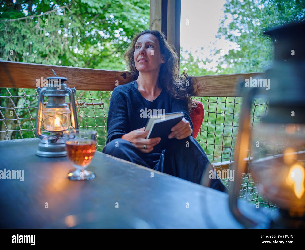 Femme mature avec le livre dans la main assis près de la lampe à huile sur le porche Banque D'Images