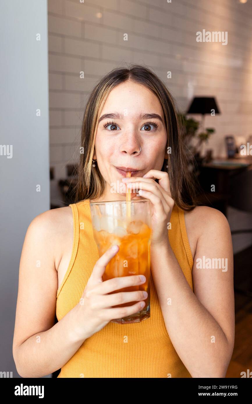 Jeune femme buvant du thé glacé avec de la paille à la maison Banque D'Images
