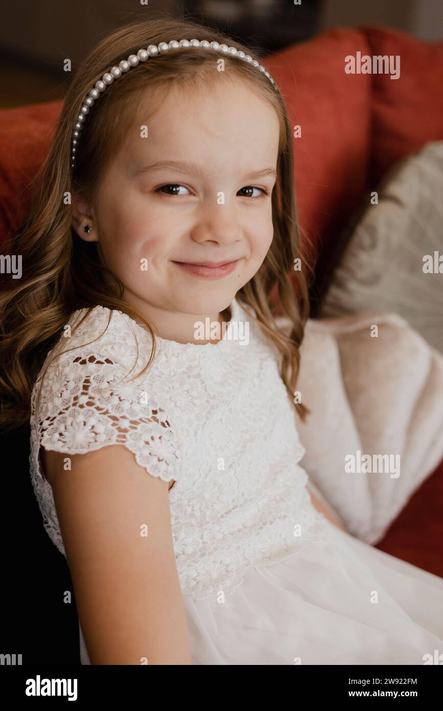 Fille souriante portant une robe blanche et assise sur le canapé Banque D'Images