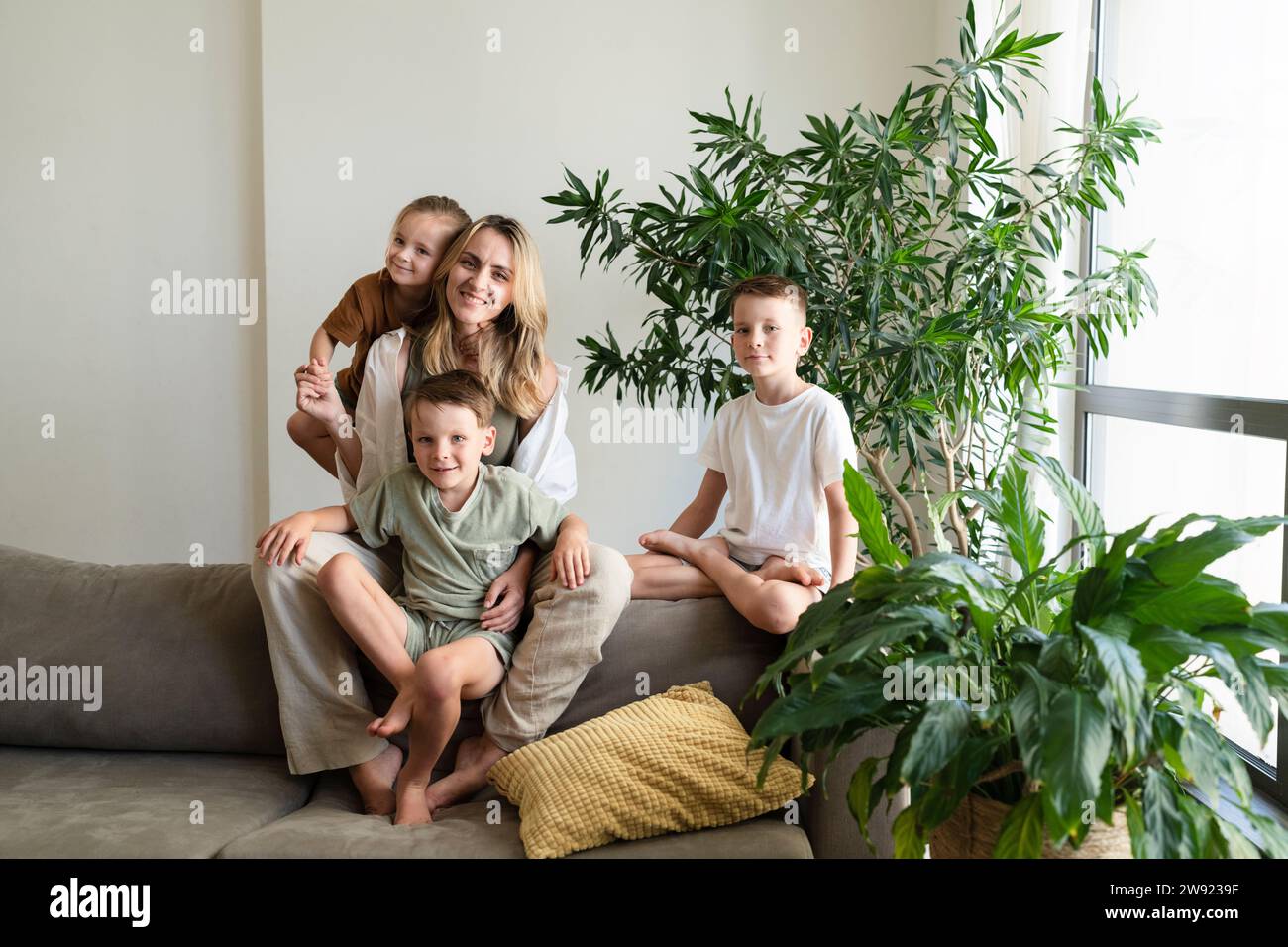 Mère blonde souriante et enfants assis sur le canapé à la maison Banque D'Images