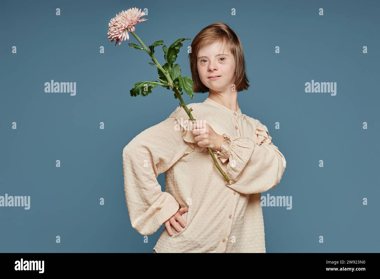 Adolescente avec le syndrome de Down tenant la fleur et posant sur fond bleu Banque D'Images