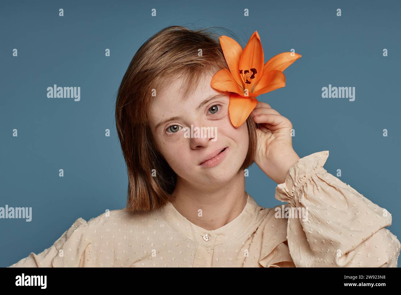 Fille avec handicap tenant orchidée orange derrière l'oreille sur fond bleu Banque D'Images