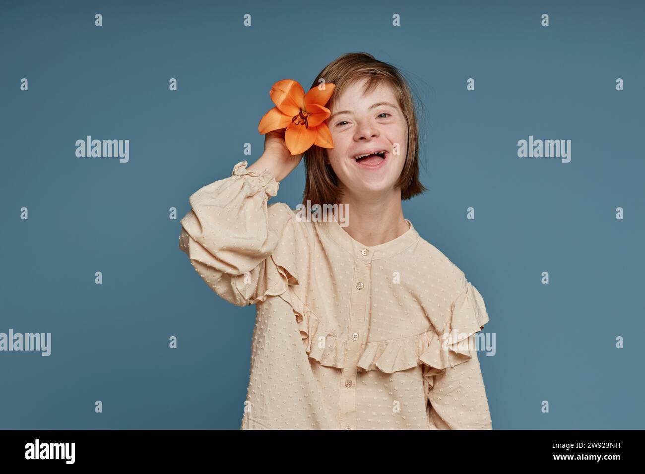 Adolescente joyeuse avec le syndrome de Down avec la fleur d'orchidée sur fond bleu Banque D'Images