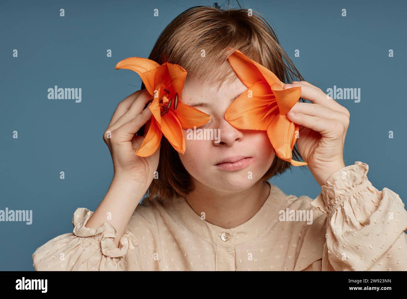Adolescente couvrant ses yeux avec des fleurs orchidées orange sur fond bleu Banque D'Images