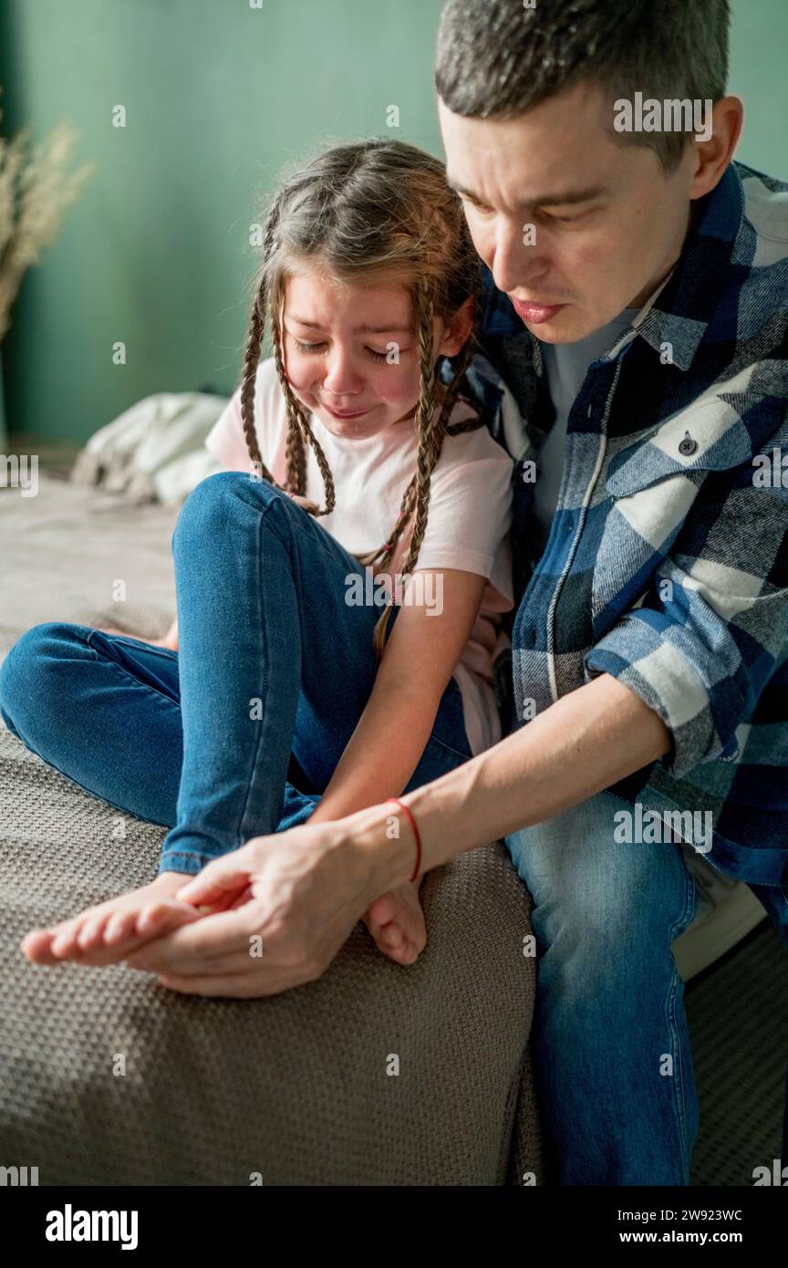 Père regardant pleurer le pied de sa fille sur le lit Banque D'Images