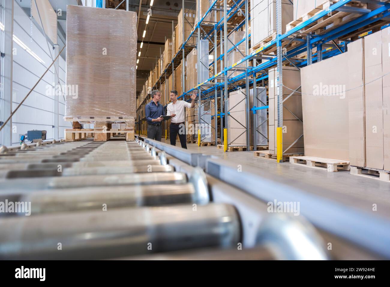 Hommes d'affaires ayant des discussions près de la bande transporteuse dans l'entrepôt Banque D'Images