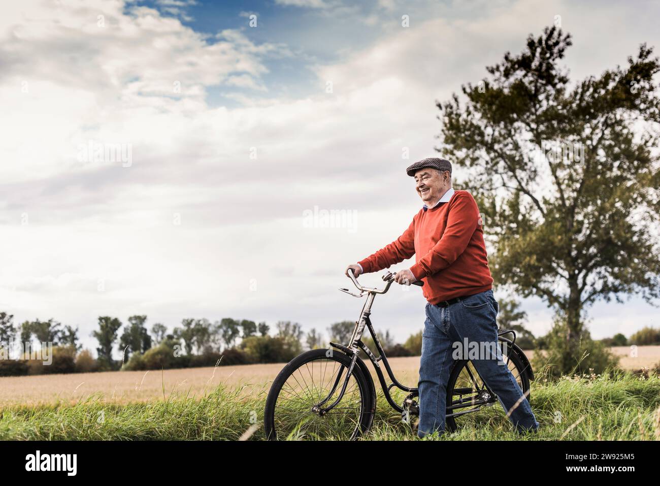 Homme âgé souriant marchant avec le vélo dans le champ Banque D'Images