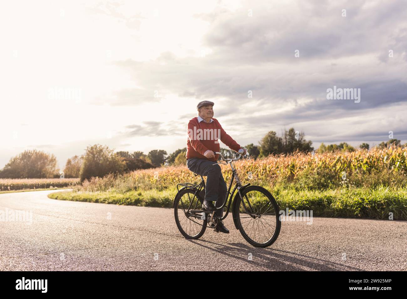 Homme senior faisant du vélo sur la route sous un ciel nuageux Banque D'Images