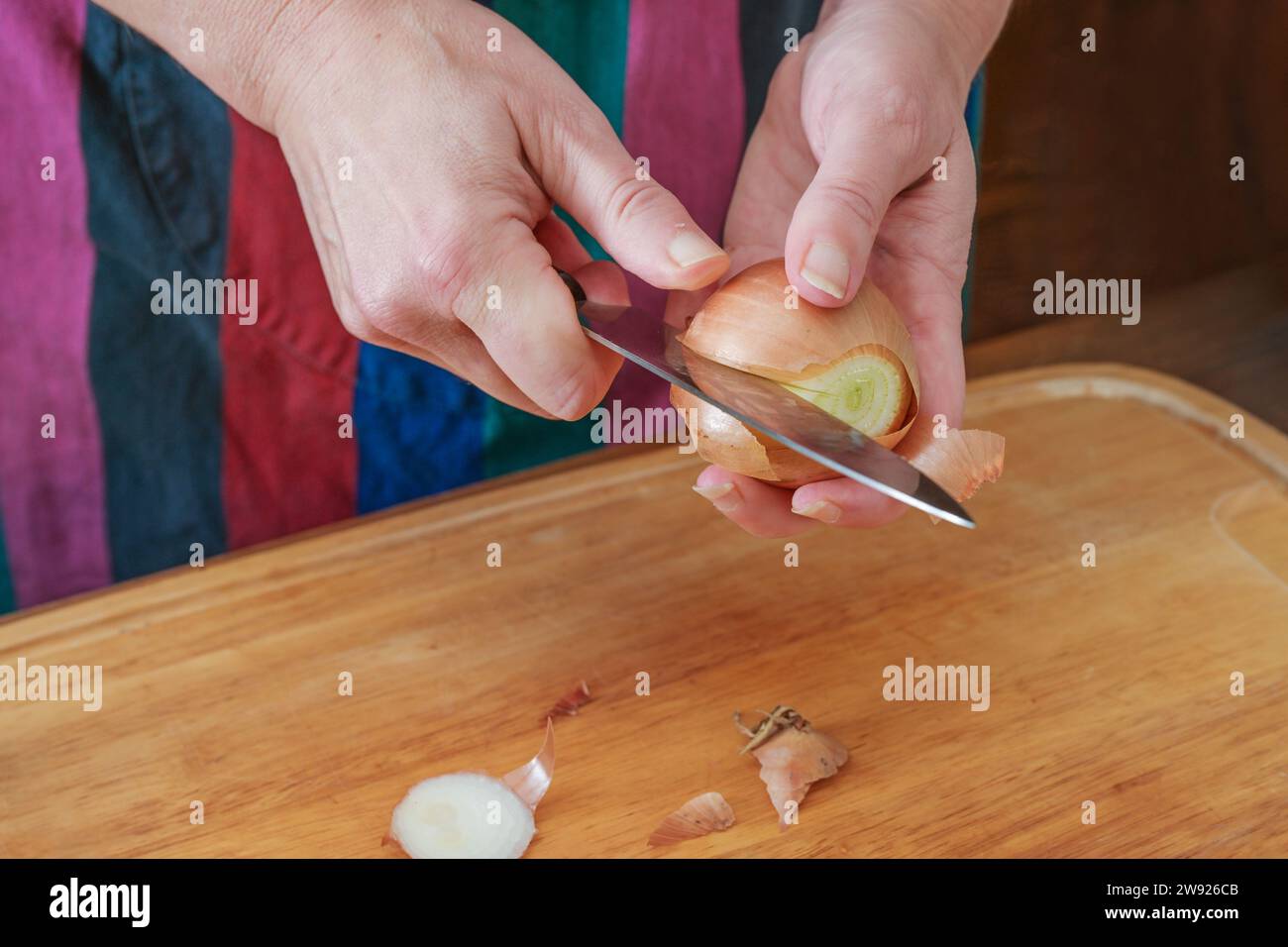 Mains d'une femme épluchant un oignon avec un couteau de cuisine au-dessus d'une planche à découper en bois, préparation pour cuisiner à la maison, espace de copie, foyer sélectionné, narr Banque D'Images