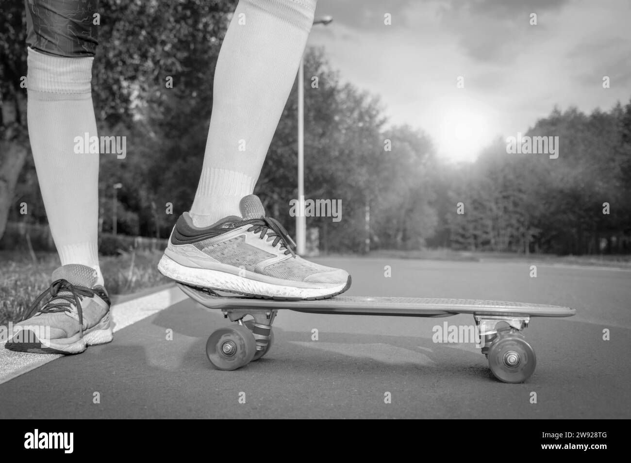 Images d'une jambe debout sur un skateboard. Soirée ensoleillée dans le parc. Concept de skateboard. Supports mixtes Banque D'Images