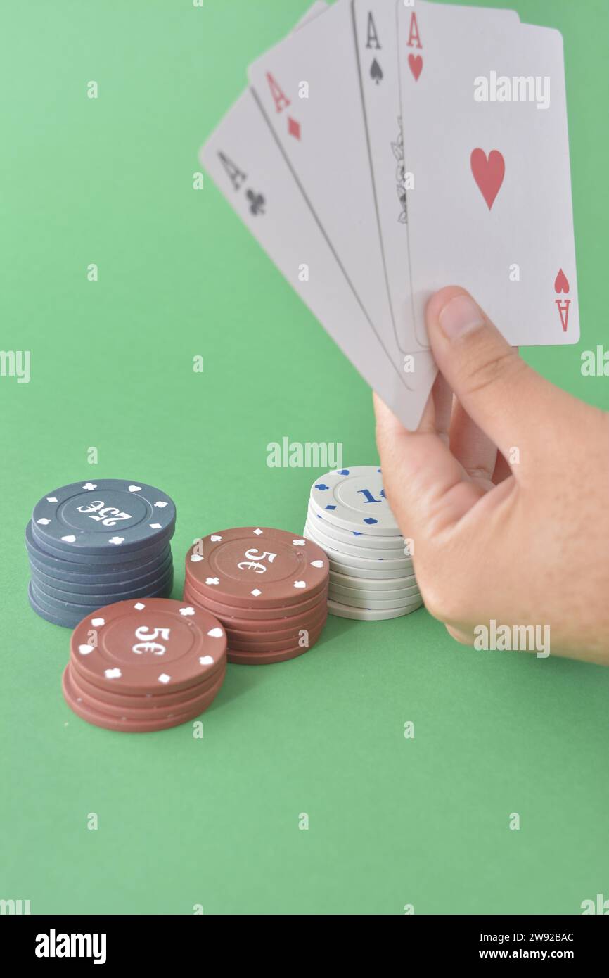 Une main présente quatre as avec des jetons de poker assortis sur fond vert, des cartes de poker et des jetons Banque D'Images