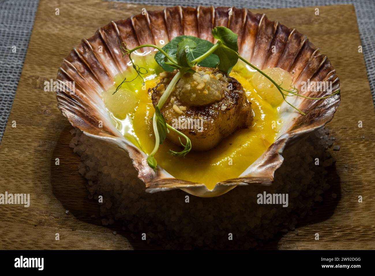 Une coquille Saint-Jacques poêlée repose avec des segments de citron et de la laitue dans sa coquille sur un lit de sel au restaurant L-Istorja du Kempinski Hotel San Lawrenz à Gozo, Malte. Une sauce jaune entoure la coquille Saint-Jacques. Banque D'Images