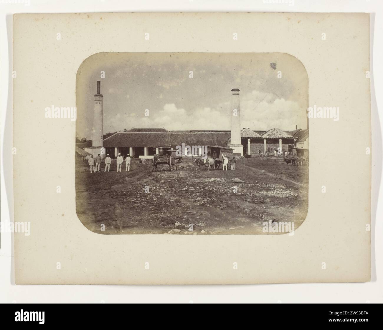 Une sucrerie, Herman Salzwedel, 1876 - 1884 photographie Une sucrerie avec deux tuyaux de cheminée, à gauche l'année 1873. Cinq Européens sont à gauche au premier plan. Au milieu, il y a trois Ossekarren avec javanais et un européen et à droite un Ossekar avec un certain nombre de Javanais en arrière-plan à l'usine. Partie de l'album photo du Surabayasche Vereeniging des fabricants de sucre offert à Frederik Beyerinck, résident de Surabaya. Surabaya support photographique albumen print Java Banque D'Images