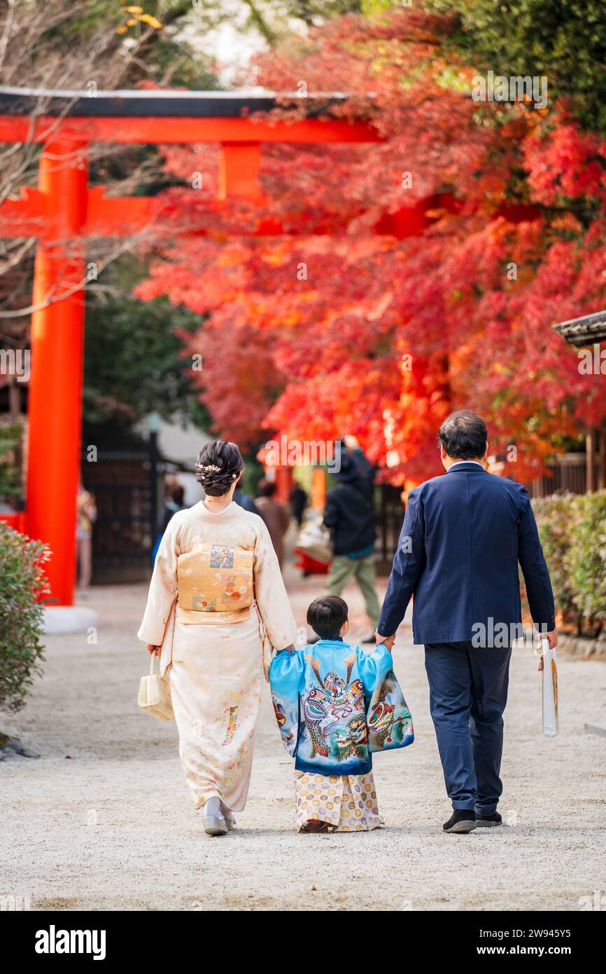 Vue arrière une famille portant un kimono traditionnel japonais dans un sanctuaire pendant la saison de l'érable d'automne. Une porte rouge Torii en arrière-plan. Banque D'Images