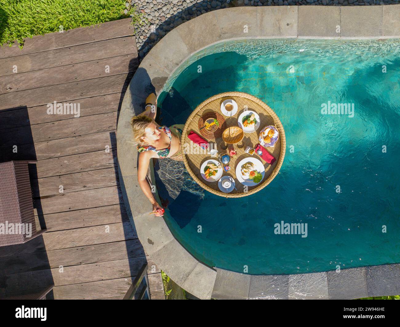 Vue aérienne d'une jeune femme prenant son petit déjeuner sur un panier flottant dans une piscine, Bali rural Banque D'Images