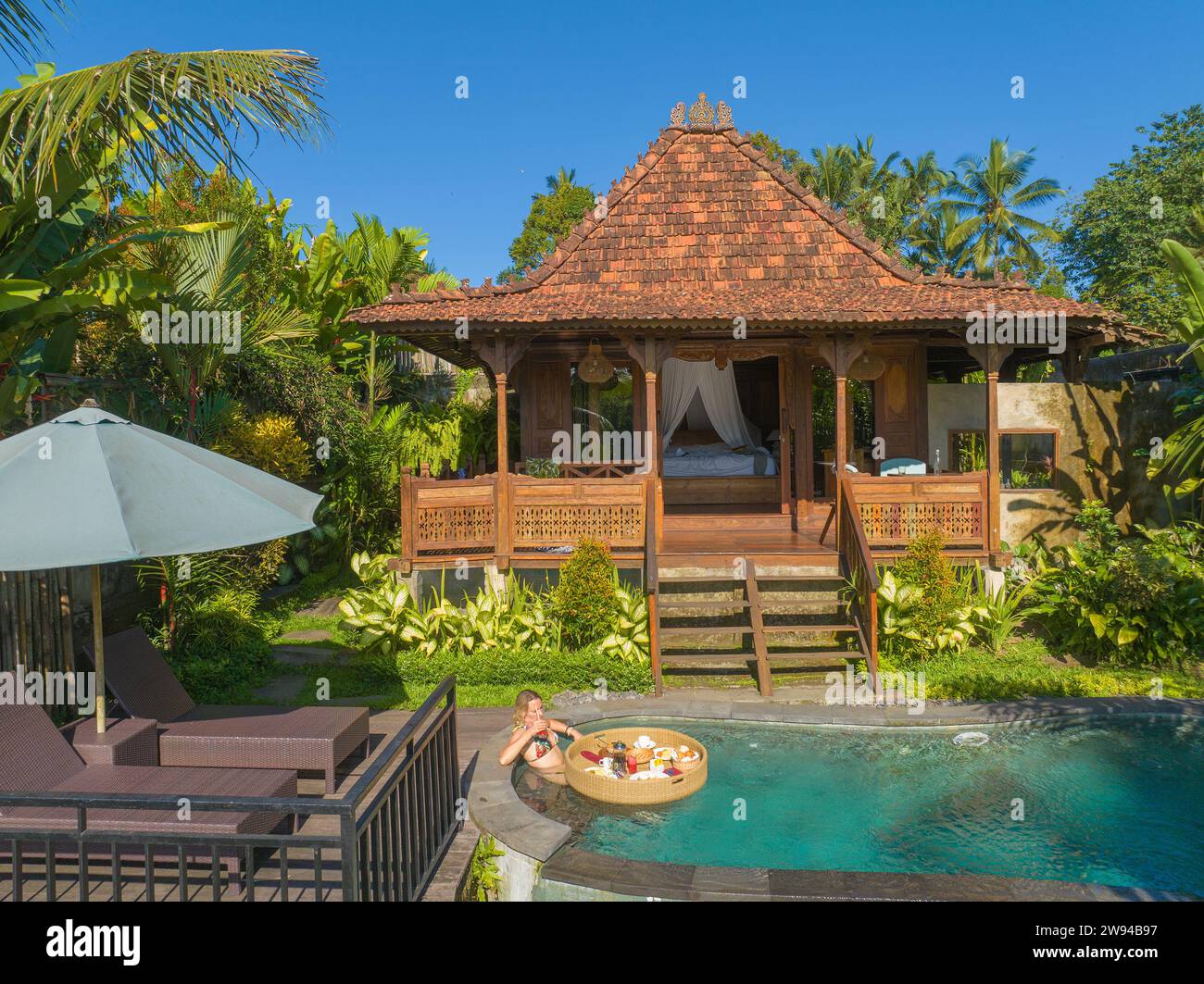 Vue aérienne d'une jeune femme prenant son petit déjeuner sur un panier flottant dans une piscine, Bali rural Banque D'Images