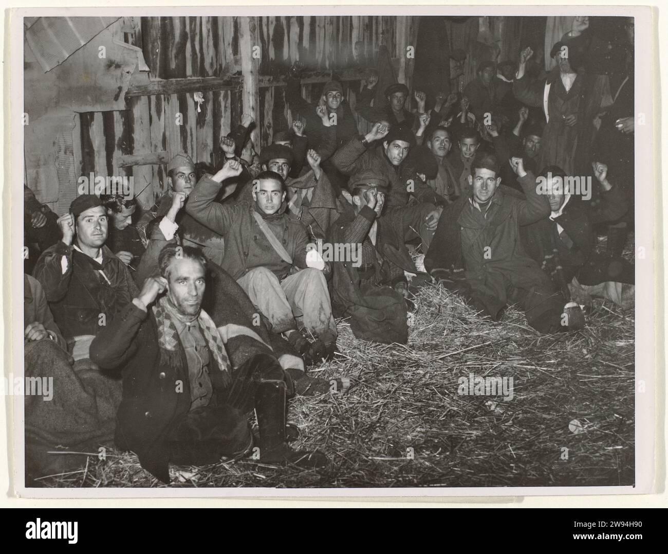 Soldats républicains au repos en France, Associated Press, photographie de 1939. Actualités photographie Un groupe de soldats républicains dans une grange de l'autre côté de la frontière française au Perthus apporte le salut communiste, le 31 janvier 1939, pendant la guerre civile espagnole. Au dos deux timbres et feuille avec texte de presse en anglais. ParisFranceAmsterdam support photographique gélatine argentique impression France Banque D'Images