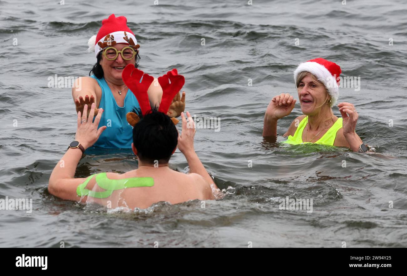 Senftenberg, Allemagne. 24 décembre 2023. Les membres du club de natation d'hiver 'Pirrlliepousen' se sont réunis pour leur traditionnelle baignade de Noël dans le lac froid de quatre degrés Senftenberg. La plupart des 25 participants se sont décorés d’un chapeau de Noël. La baignade de Noël a lieu depuis 36 ans - à l'exception de deux ans liés au coronavirus. 'Pirrlliepousen' est un terme nord-allemand pour désigner les glaçons. Crédit : Bernd Wüstneck/dpa/Alamy Live News Banque D'Images