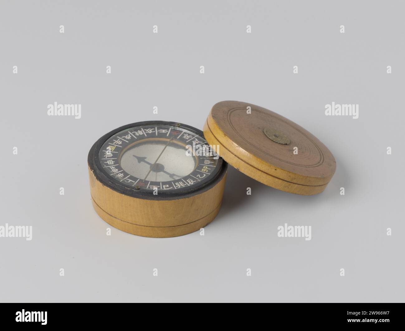 Boussole chinoise, PAE Sze Co., 1850 - 1899 boussole boussole chinoise composée d'un bol, peint en blanc à l'intérieur et recouvert de verre, contenant une aiguille de boussole sèche. Les boussoles chinoises ont une subdivision en 24 directions de vent. Les directions du vent sont indiquées en caractères blancs, le nord et le sud sont indiqués en rouge, l'est et l'ouest en Geel. Noord-Zuid est également représenté par un fil métallique. Sur l'intérieur du couvercle est un timbre avec le nom du fabricant PAE Sze Co. De Chefoo, l'actuel Yantai. Bois de Yantai (matière végétale). verre. métal. cuivre (métal) Banque D'Images