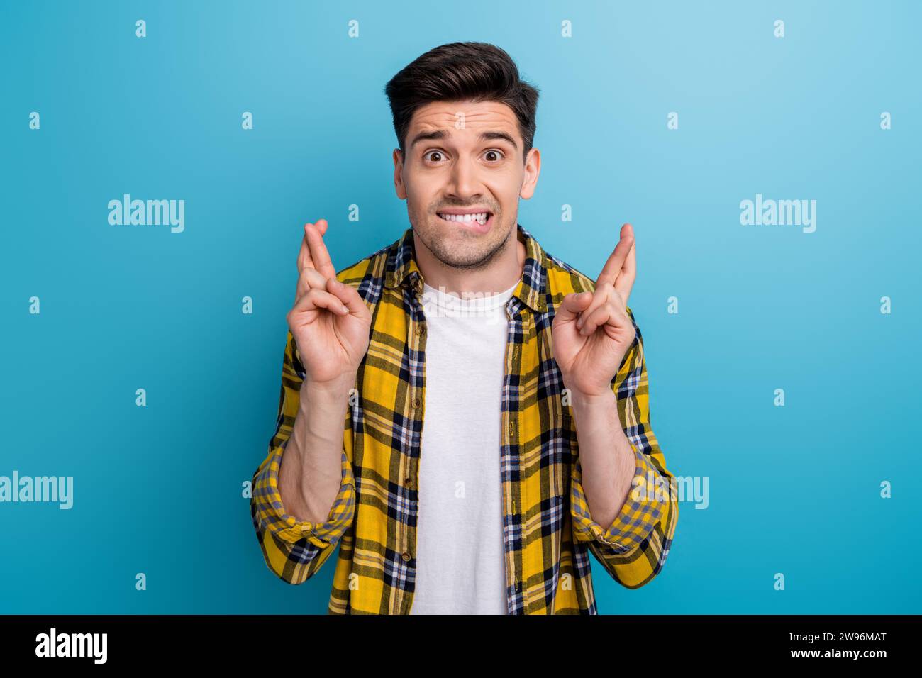 Portrait de jeune homme dans une chemise à carreaux élégante doigts croisés prier mordre les lèvres attendez-vous à de meilleurs résultats isolés sur fond de couleur bleue Banque D'Images