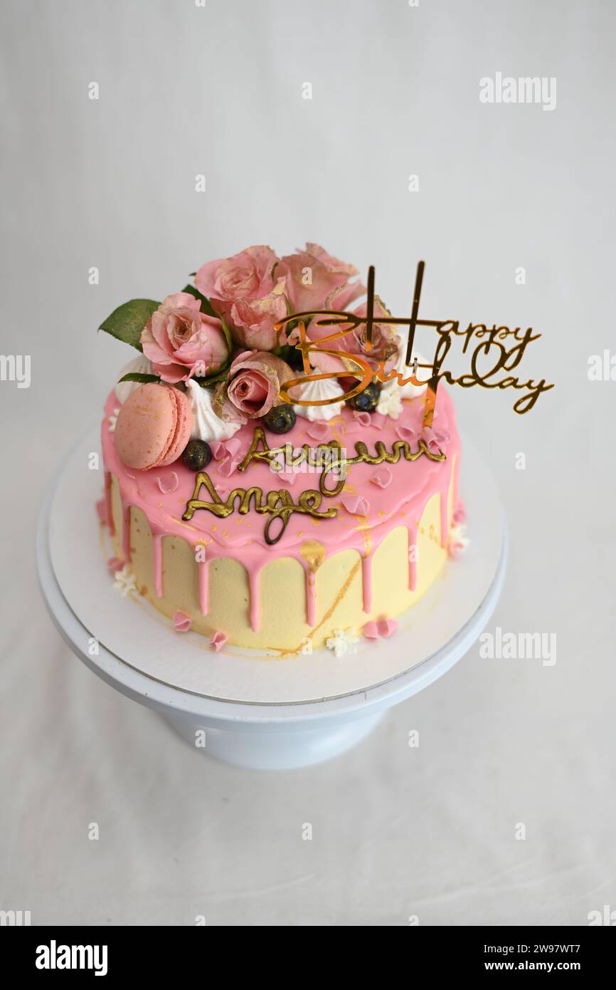glaçage givré frais égouttant gâteau d'anniversaire rose vanille vraies roses et décoration macaron sur le dessus avec signe doré Banque D'Images