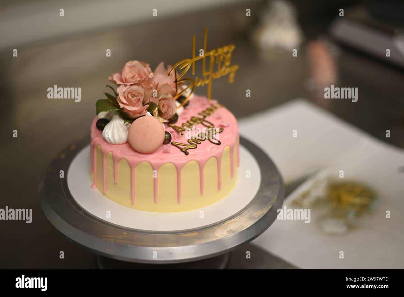 glaçage givré frais égouttant gâteau d'anniversaire rose vanille vraies roses et décoration macaron sur le dessus avec signe doré Banque D'Images