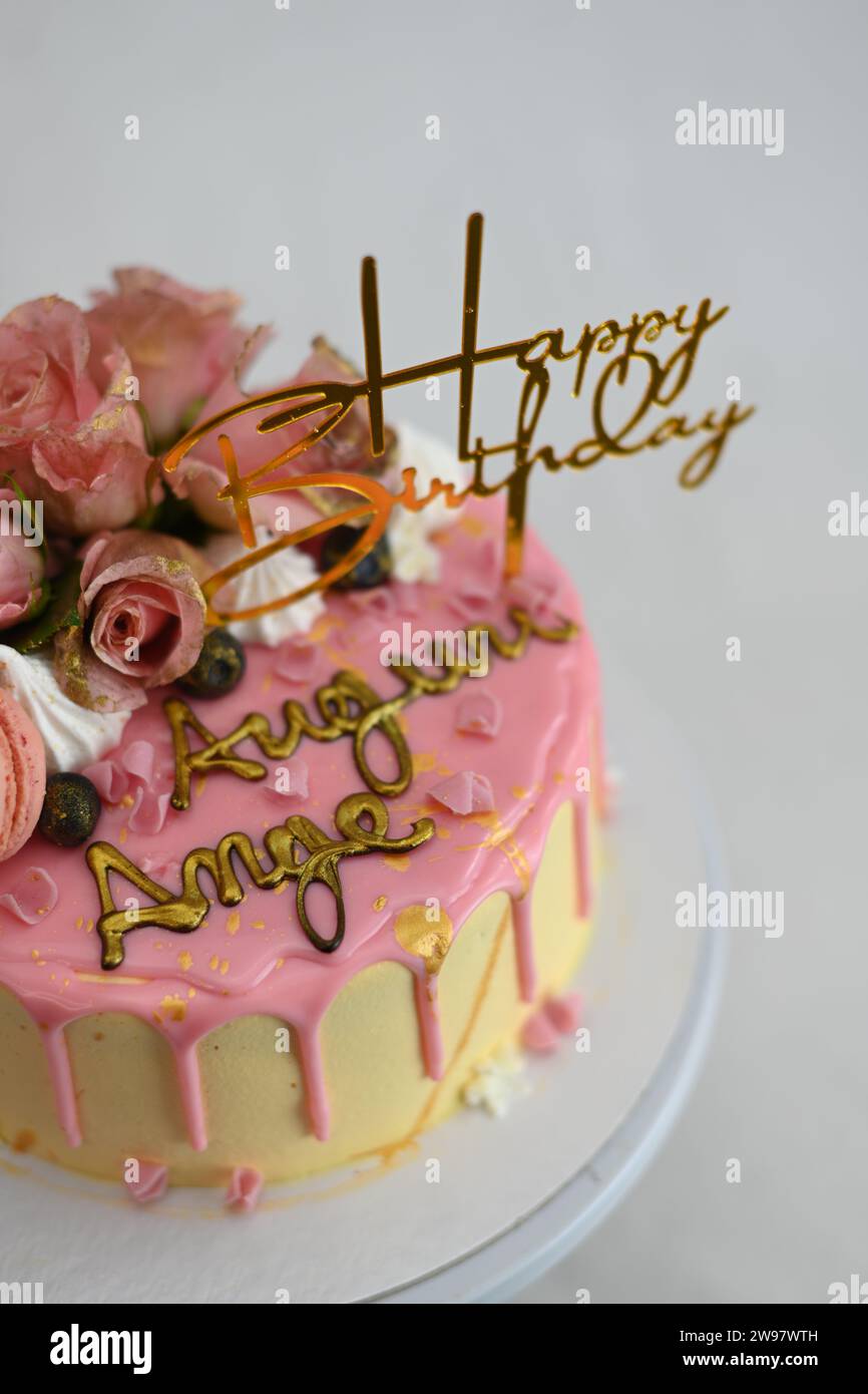 glaçage givré frais égouttant gâteau d'anniversaire rose vanille vraies roses et décoration macaron sur le dessus avec signe doré Banque D'Images