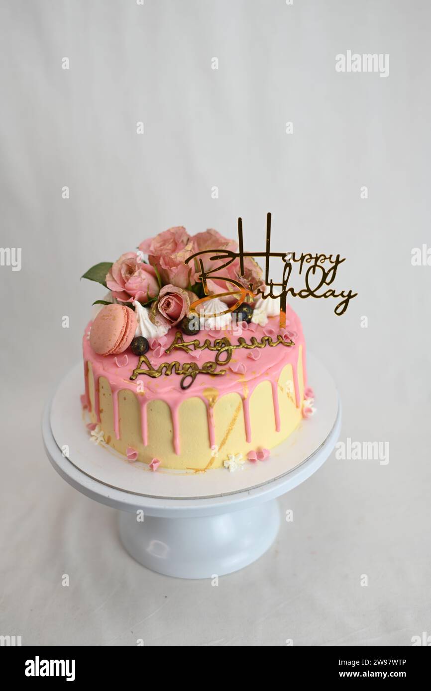 glaçage givré frais égouttant gâteau d'anniversaire rose vanille vraies roses et décoration macaron sur le dessus avec signe doré Banque D'Images