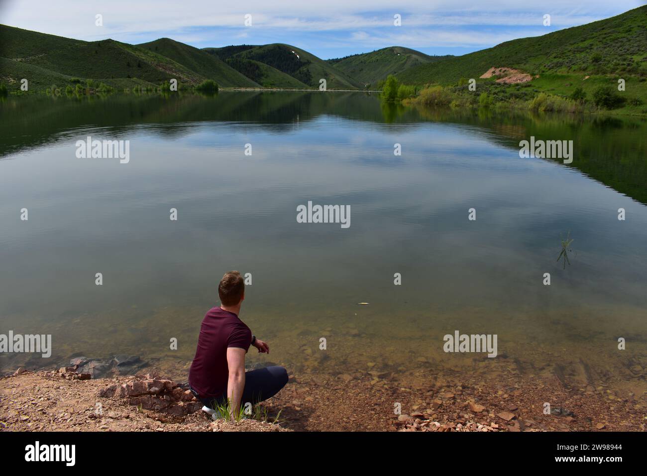 Jeune athlète vêtu d'un t-shirt bordelais accroupi au bord du réservoir de Montpellier et regardant l'eau plate Banque D'Images