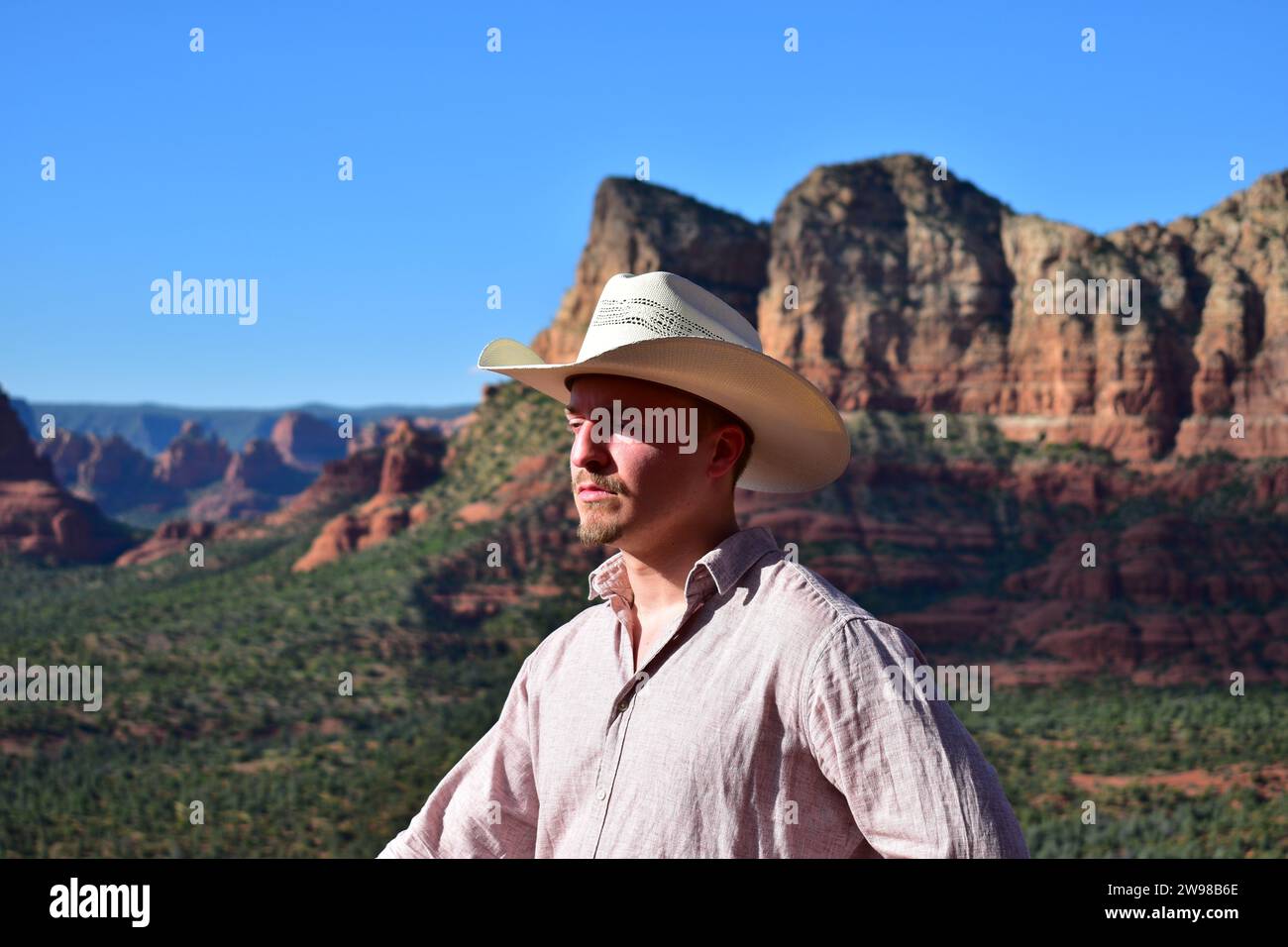 Homme en chemise rose et portant un chapeau de cow-boy blanc avec le paysage de Sedona dans le désert de l'Arizona comme arrière-plan Banque D'Images