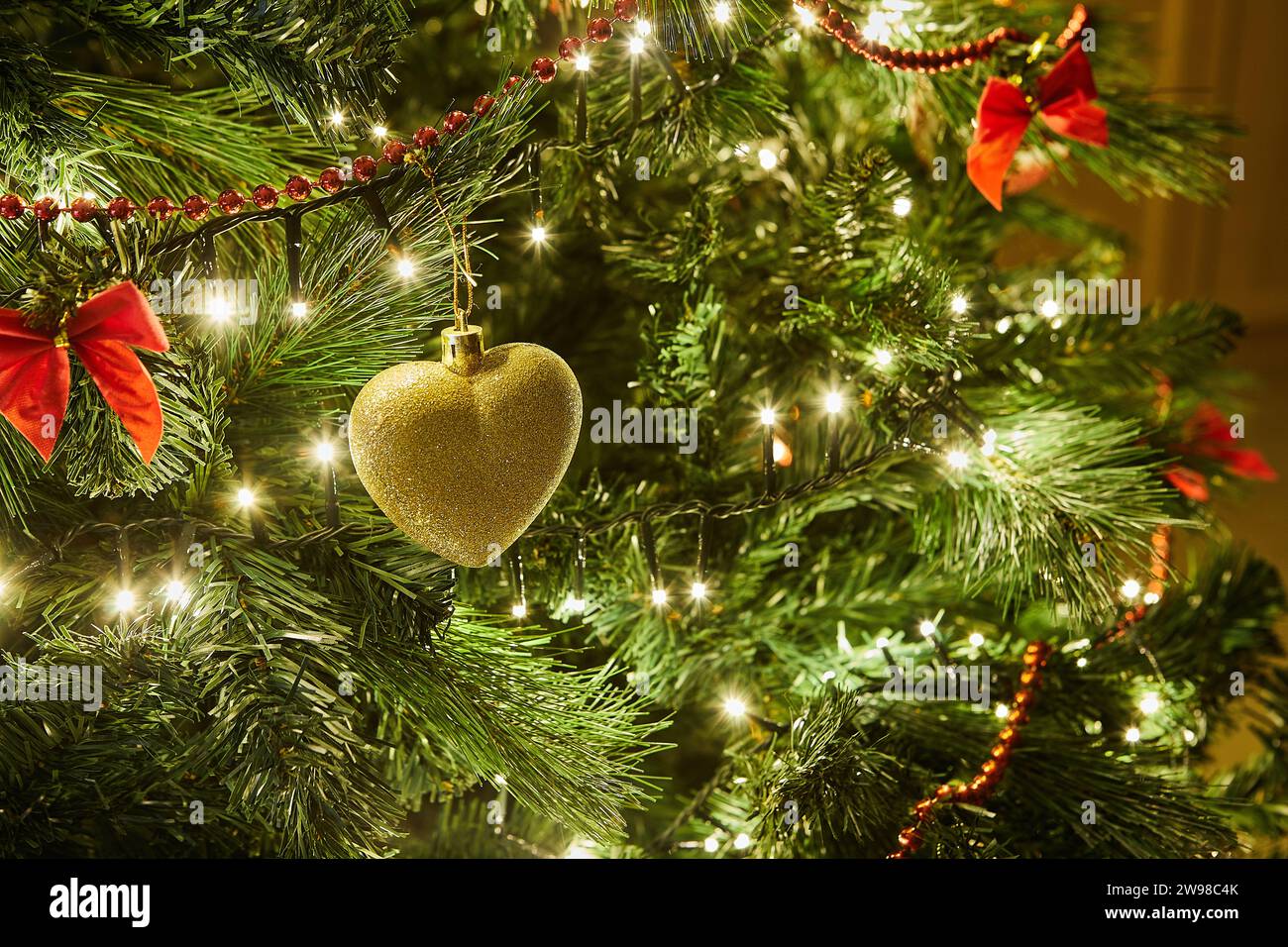 Gros plan d'un sapin de Noël magnifiquement décoré avec des ornements colorés, une guirlande scintillante et des lumières brillantes, créant un cadre festif et magique Banque D'Images