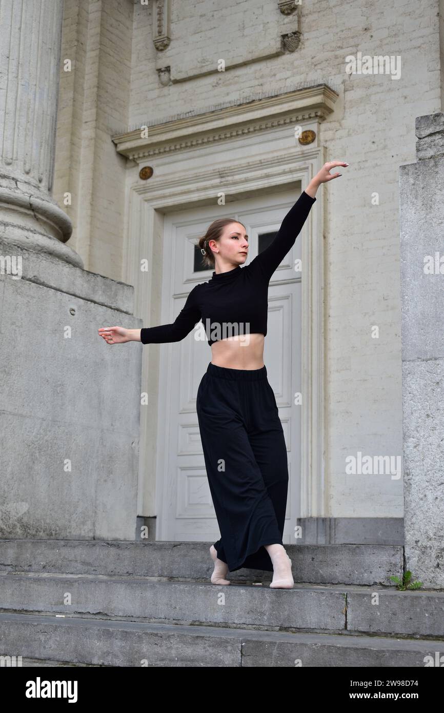Jeune femme en tenue noire effectuant un mouvement de danse contemporaine sur des escaliers en pierre Banque D'Images