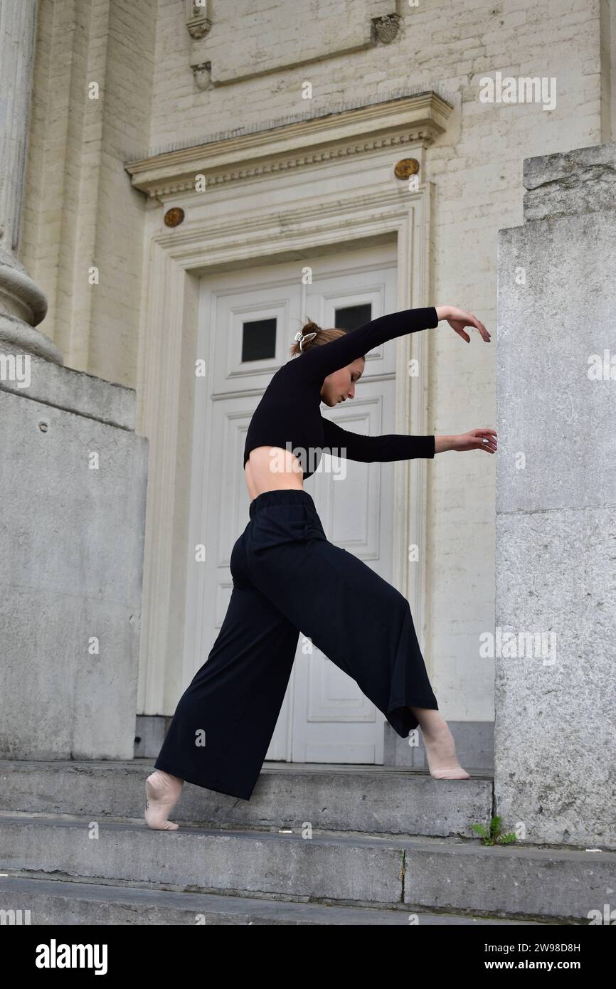 Jeune femme en tenue noire effectuant un mouvement de danse contemporaine sur des escaliers en pierre Banque D'Images