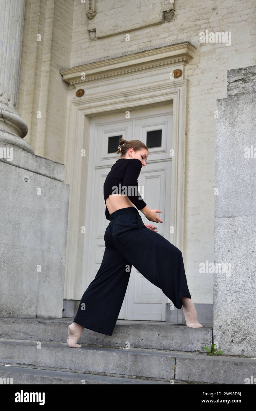 Jeune femme en tenue noire effectuant un mouvement de danse contemporaine sur des escaliers en pierre Banque D'Images